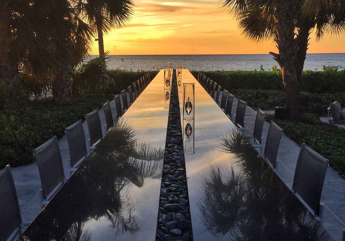 Colorful sunset off the edge of the Caribbean's longest bar, Grace Bay Club's Infinity Bar. The long bar is black mirror and reflects the sunset and palm trees.